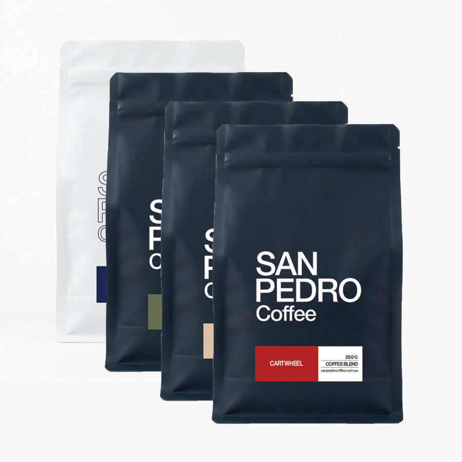 Four black San Pedro Coffee bag packages arranged in a staggered row on a light grey background, with different label colours and roast names including Ethiopian Yirgacheffe, San Pedro Coffee Catamaran, San Pedro Coffee Sumatra, and San Pedro Coffee Colombia.