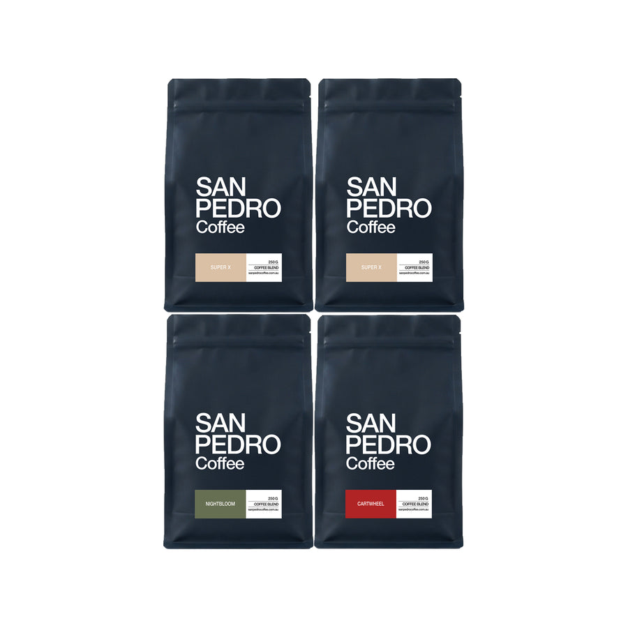 Four San Pedro Coffee bags arranged in a 2x2 grid on a white background. The bags are dark navy blue with white text, and each has a small color-coded flavor label: red for Caramel, gray for DECAF, olive green for Nightshade, and beige for Lupin.