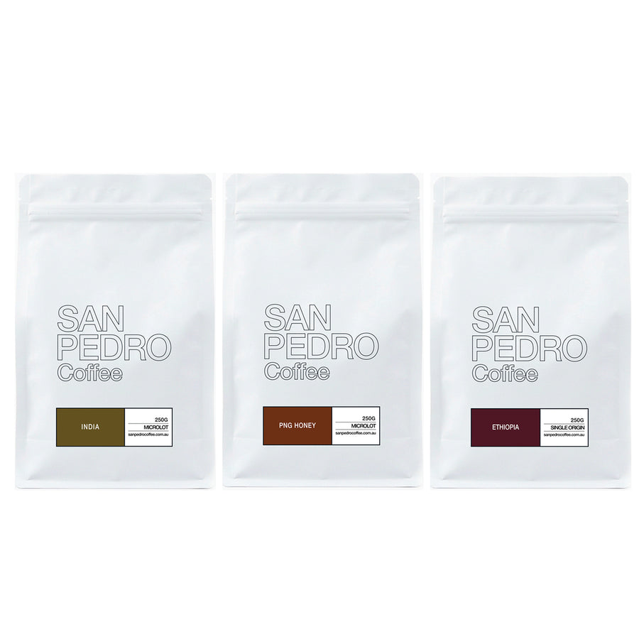Three white stand-up coffee bags from San Pedro Coffee lined up side by side on a white background. The bags feature different flavor labels: India, Pils Honey, and Ethiopia, each with a small color block representing the coffee's origin.