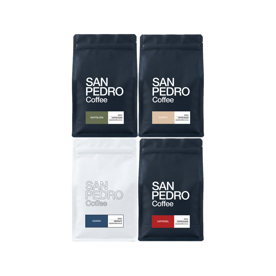 Four San Pedro Coffee stand-up pouches arranged in a 2x2 grid on a white background. The top two are dark navy with white text and small green/beige label blocks, and the bottom two are white and navy with blue/red label blocks.